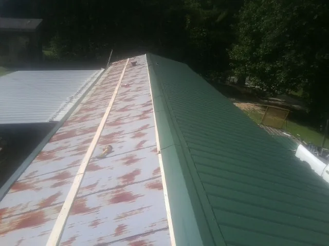 Old rusted panels beside newly installed green metal roofing — Wind Damage Roof Repair by Roofing Brothers in Carencro