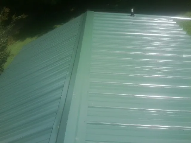 New green metal panels meeting at the ridge of a roof — Flat Roof Repair work by our crew in Carencro