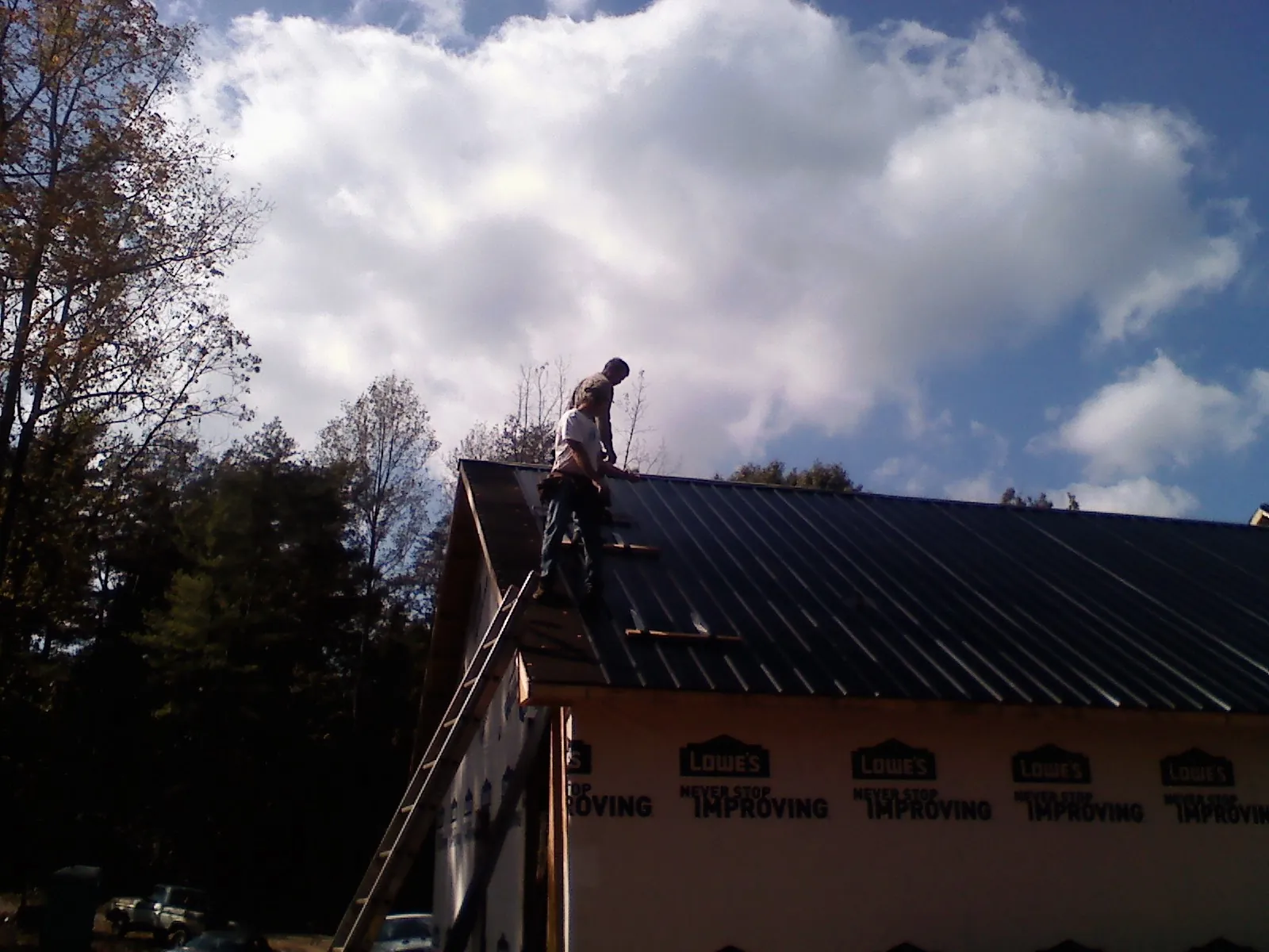 Roofer fastening dark metal panels high against a cloudy sky, from a Roof Inspection job in Carencro