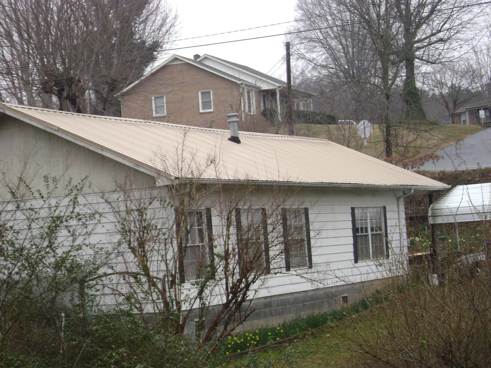 Tan metal roof on a white sided house set into a hillside — Commercial Roofing by Roofing Brothers in Carencro