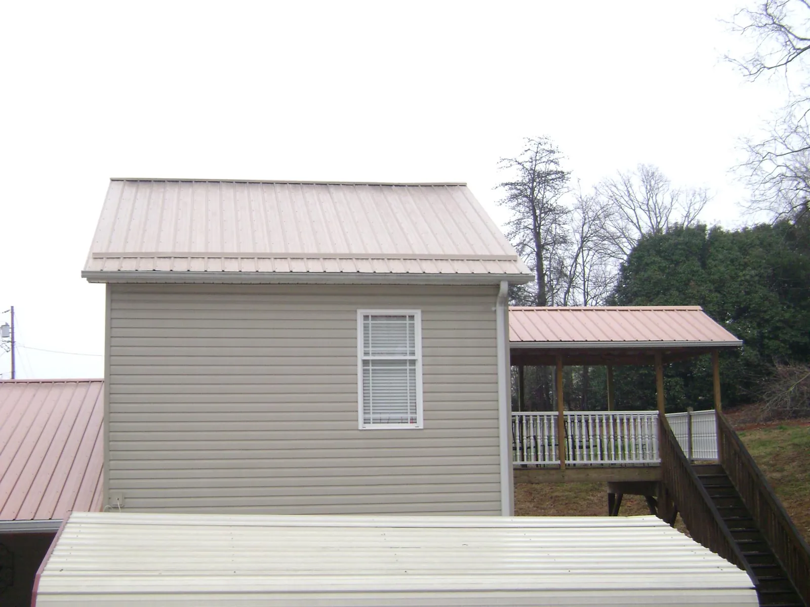 Tan metal roofs on a two story addition and attached porch, from a Roof Replacement job in Carencro